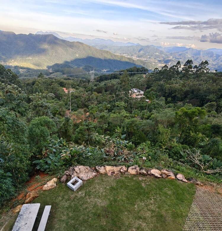 Jardim visto de cima, com mesa de piquenique em pedra e fogueira, cercado pela Mata Atlântica ao entardecer.