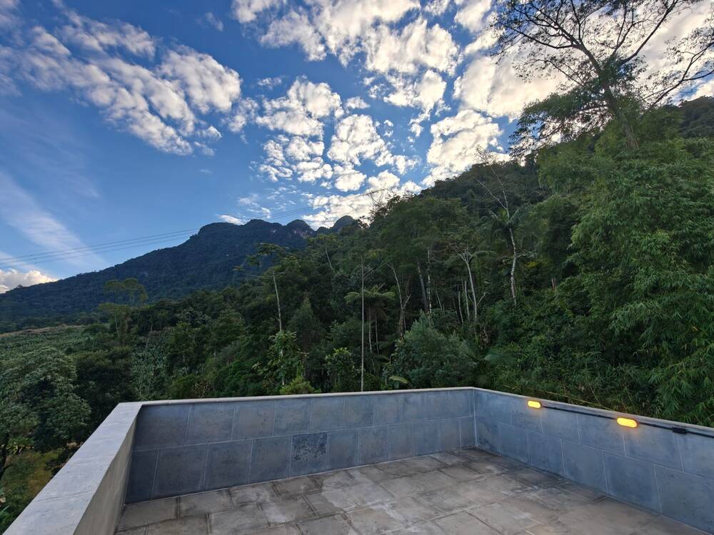 Vista do terraço para um pico rochoso coberto de mata, sob um céu azul com nuvens.
